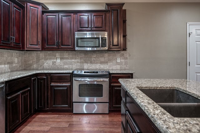 kitchen with dark brown cabinetry, tasteful backsplash, appliances with stainless steel finishes, dark hardwood / wood-style flooring, and light stone countertops