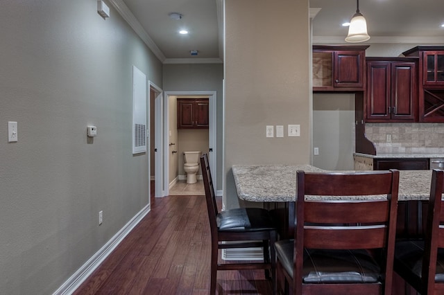 kitchen with a breakfast bar area, light stone counters, ornamental molding, pendant lighting, and decorative backsplash