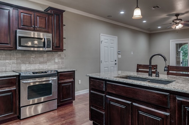 kitchen featuring sink, backsplash, hanging light fixtures, stainless steel appliances, and light stone counters