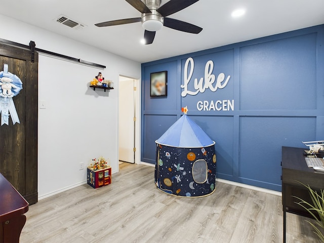 game room with ceiling fan, a barn door, and light hardwood / wood-style flooring