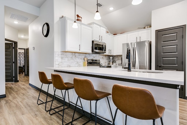 kitchen with pendant lighting, stainless steel appliances, light countertops, white cabinets, and a peninsula