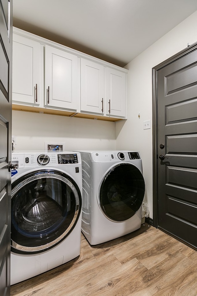 clothes washing area featuring light wood finished floors, separate washer and dryer, and cabinet space