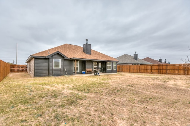 back of house with a fenced backyard, a chimney, a lawn, and a patio