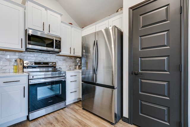 kitchen with vaulted ceiling, white cabinetry, stainless steel appliances, and light countertops