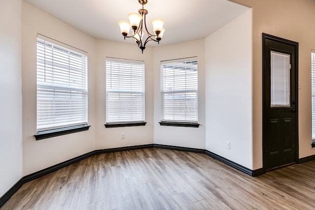 empty room featuring baseboards, a notable chandelier, and light wood finished floors