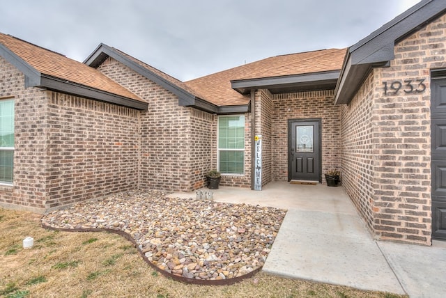 property entrance with roof with shingles, a patio, and brick siding