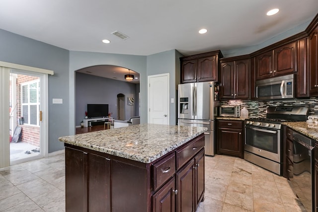 kitchen with visible vents, light stone counters, arched walkways, backsplash, and stainless steel appliances