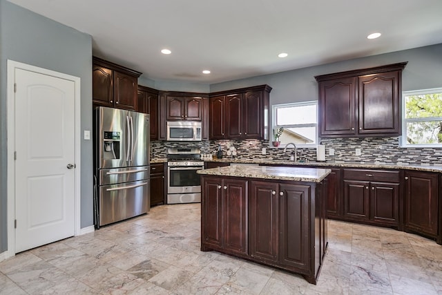 kitchen featuring stainless steel appliances, light stone countertops, dark brown cabinets, and tasteful backsplash
