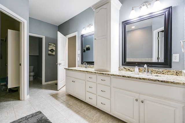 full bathroom with baseboards, double vanity, a sink, and toilet