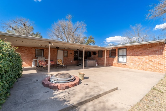 back of house with a patio area, a hot tub, a fire pit, and brick siding