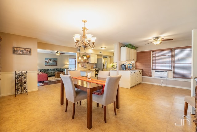 dining room with a wealth of natural light, wainscoting, cooling unit, and ceiling fan with notable chandelier