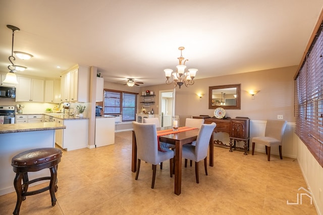 dining room with ceiling fan with notable chandelier, a wainscoted wall, and light tile patterned flooring