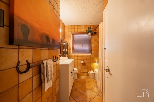 bathroom with a textured ceiling, toilet, vanity, tile walls, and tile patterned floors