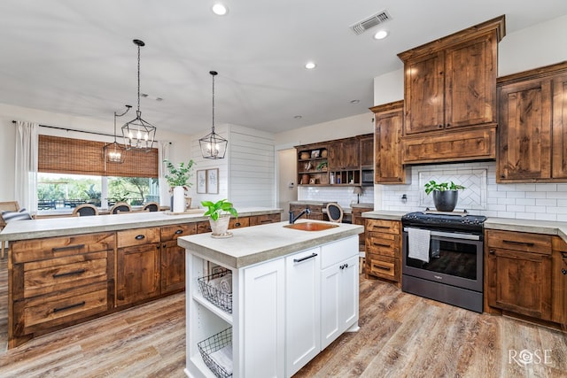 kitchen with decorative light fixtures, white cabinets, backsplash, stainless steel range, and a center island with sink