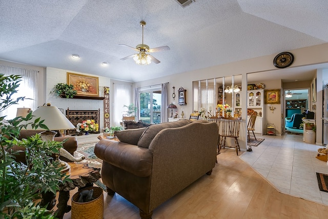 living room featuring vaulted ceiling, a large fireplace, ceiling fan, a textured ceiling, and light hardwood / wood-style flooring