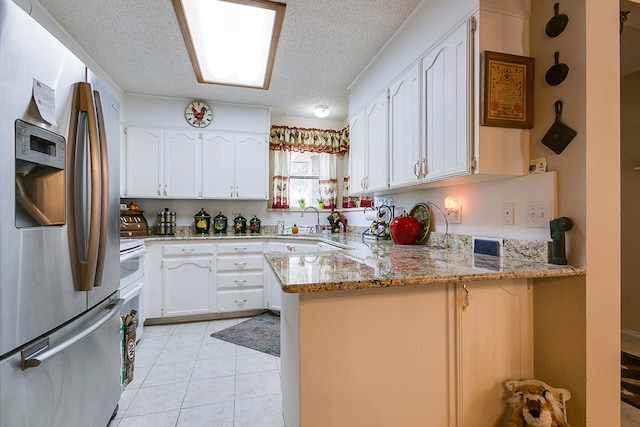 kitchen with light tile patterned flooring, white cabinets, stainless steel fridge, kitchen peninsula, and light stone countertops