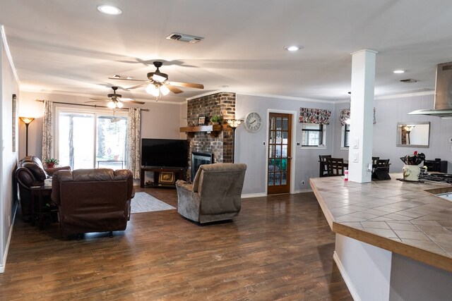 living room with dark wood-type flooring, ceiling fan, ornamental molding, and a fireplace