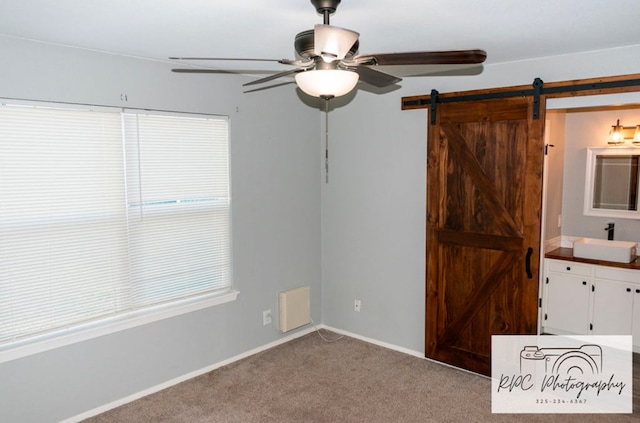 unfurnished bedroom with sink, light colored carpet, a barn door, and ceiling fan