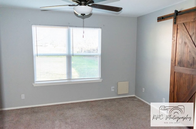 carpeted spare room with plenty of natural light, a barn door, and ceiling fan