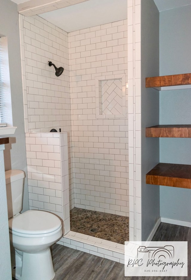 bathroom featuring hardwood / wood-style flooring, toilet, and a tile shower