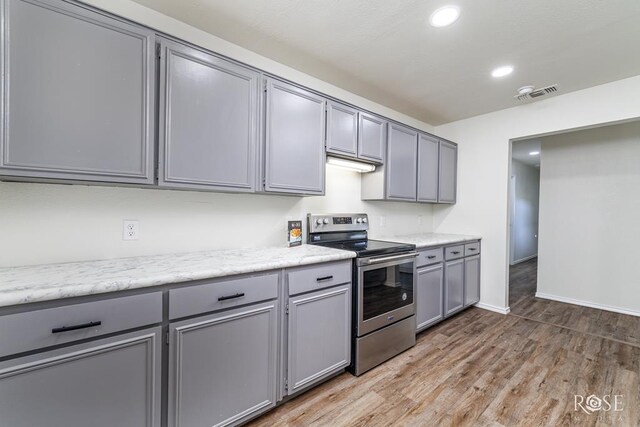 kitchen with electric stove, gray cabinets, light stone countertops, and hardwood / wood-style flooring