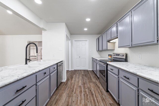 kitchen featuring appliances with stainless steel finishes, dark hardwood / wood-style floors, sink, gray cabinetry, and light stone countertops