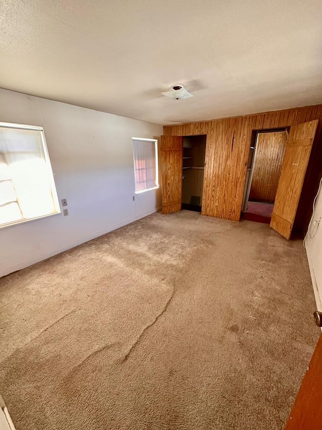 unfurnished bedroom featuring a textured ceiling, two closets, wood walls, and light carpet