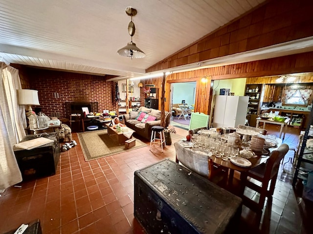 dining room featuring vaulted ceiling, a brick fireplace, wooden walls, dark tile patterned floors, and brick wall