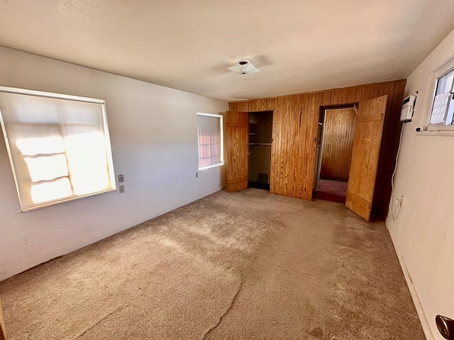 unfurnished bedroom with wooden walls, multiple windows, and carpet