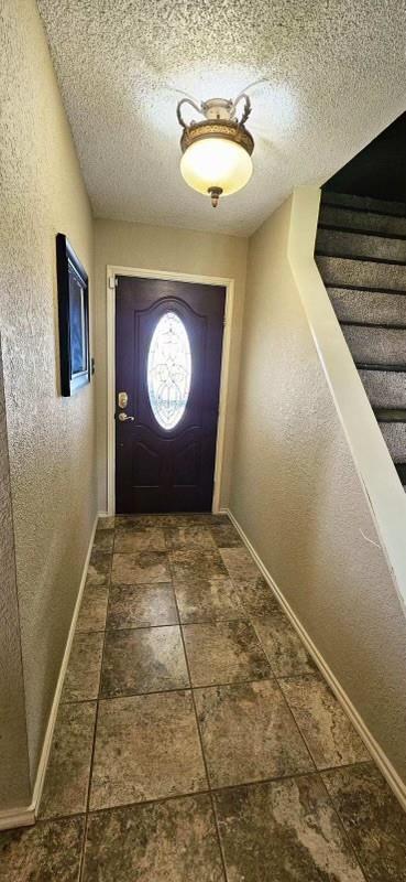 1210 Elizabeth St, Rankin, TX 79778 - doorway to outside featuring baseboards, a textured wall, a textured ceiling, and stairs