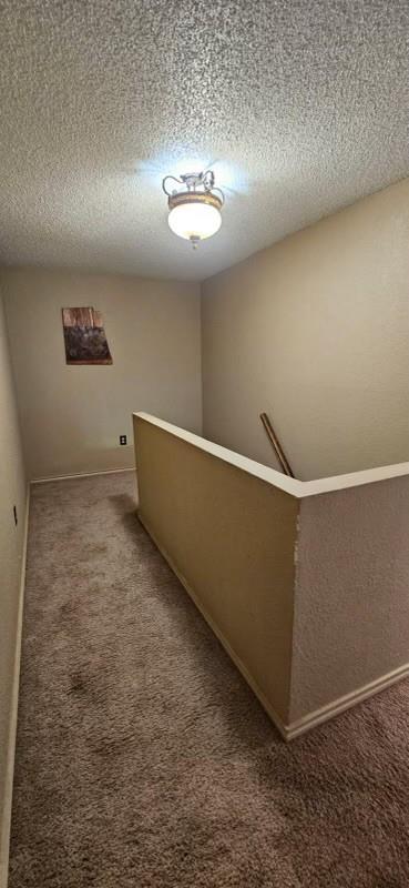 1210 Elizabeth St, Rankin, TX 79778 - corridor featuring carpet, a textured ceiling, an upstairs landing, and baseboards