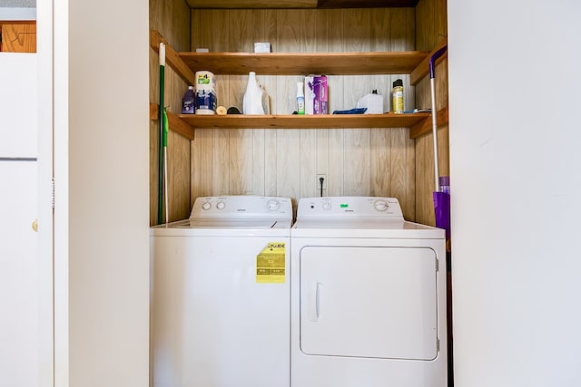 clothes washing area with washing machine and clothes dryer and wood walls