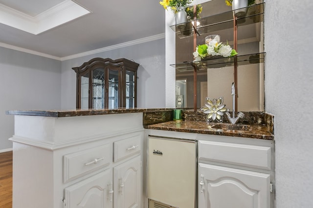 bar with white cabinetry, wood-type flooring, sink, dark stone countertops, and ornamental molding