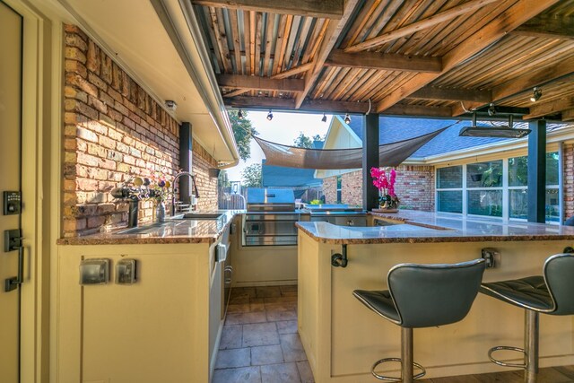 kitchen with sink, beam ceiling, a kitchen breakfast bar, brick wall, and kitchen peninsula