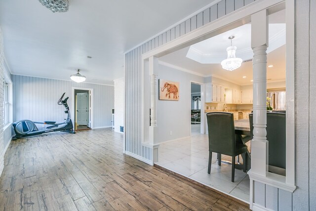 interior space featuring decorative columns, ornamental molding, a notable chandelier, and light wood-type flooring