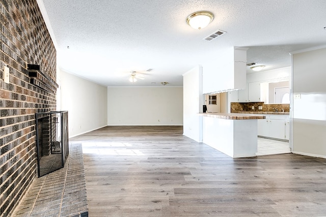 2410 Louise Dr, San Angelo, TX 76901 - unfurnished living room featuring a textured ceiling, a fireplace, ceiling fan, light wood-type flooring, and crown molding
