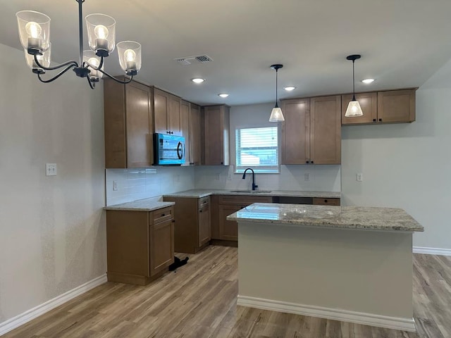 kitchen featuring sink, backsplash, a center island, light stone countertops, and light hardwood / wood-style floors