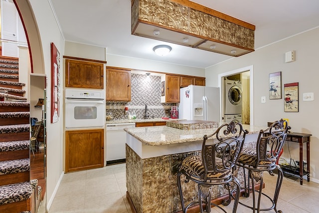 4918 Blue Ridge Trl, San Angelo, TX 76904 - kitchen with decorative backsplash, stacked washer / dryer, white appliances, a breakfast bar area, and light tile patterned floors