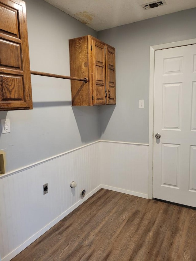 laundry room featuring wainscoting, cabinet space, electric dryer hookup, and dark wood-type flooring