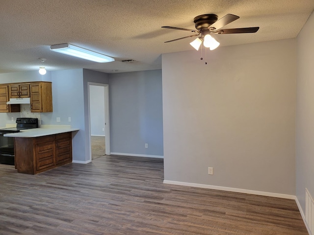 kitchen with under cabinet range hood, black electric range oven, a peninsula, and dark wood-style flooring