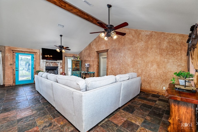 living room with ceiling fan, a stone fireplace, and lofted ceiling with beams