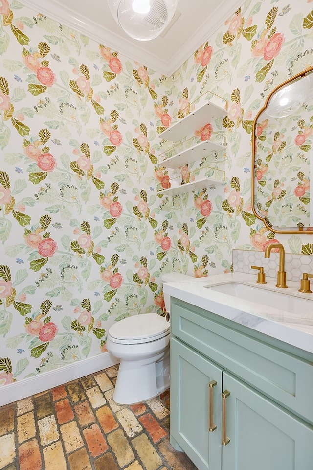 bathroom featuring toilet, baseboards, wallpapered walls, crown molding, and vanity