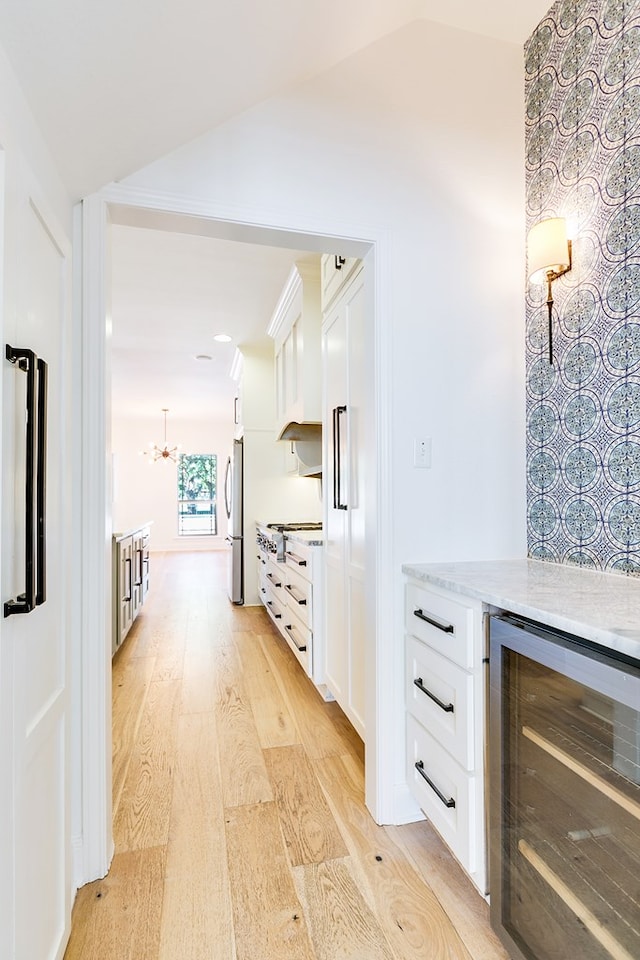 interior space featuring lofted ceiling, an inviting chandelier, beverage cooler, and light wood-style floors