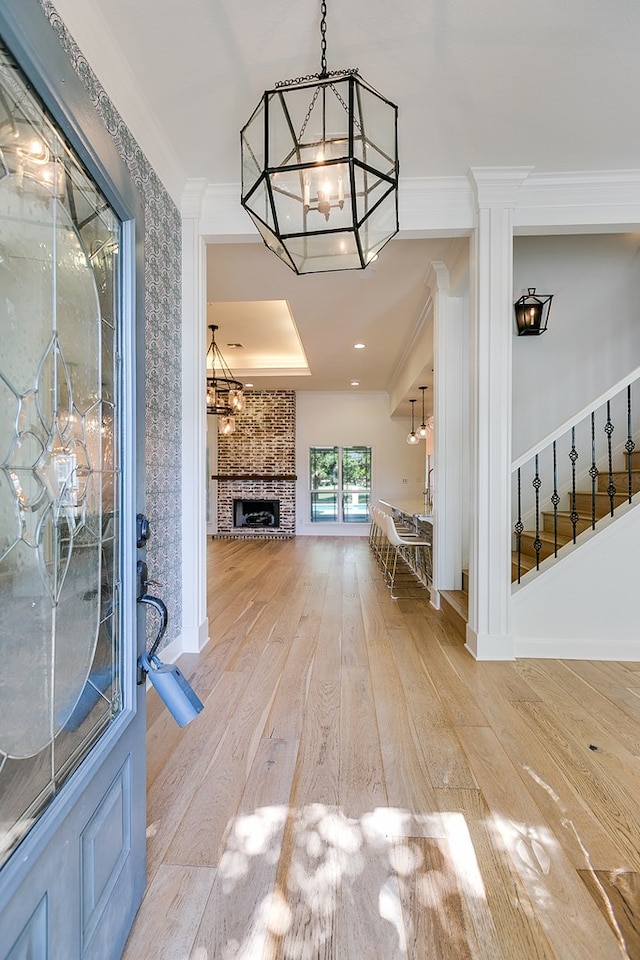 foyer featuring hardwood / wood-style floors, stairway, crown molding, a chandelier, and a large fireplace