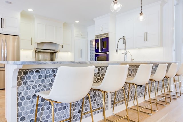 kitchen with multiple ovens, a breakfast bar, light wood finished floors, white cabinets, and freestanding refrigerator