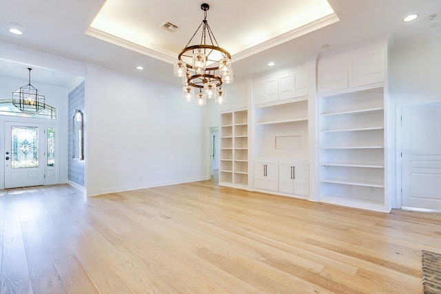 interior space with a tray ceiling, visible vents, ornamental molding, light wood-style floors, and a notable chandelier