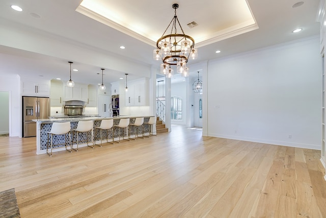 kitchen with a kitchen breakfast bar, an inviting chandelier, a raised ceiling, visible vents, and stainless steel refrigerator with ice dispenser