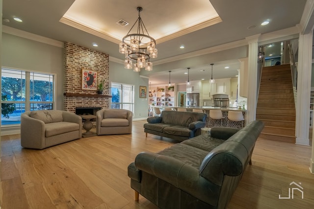 living room featuring a brick fireplace, light wood-type flooring, and a tray ceiling