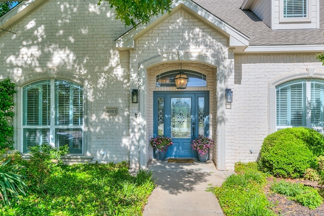 view of exterior entry with brick siding and a shingled roof