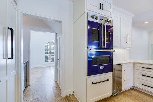 kitchen featuring ornamental molding, light wood-style flooring, tasteful backsplash, multiple ovens, and white cabinetry